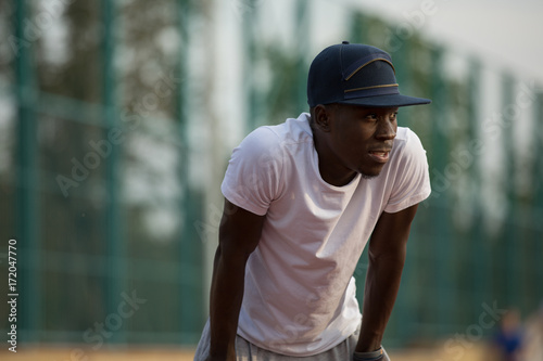 African male sportsman in a cap workout outside, he hardy breathe after running