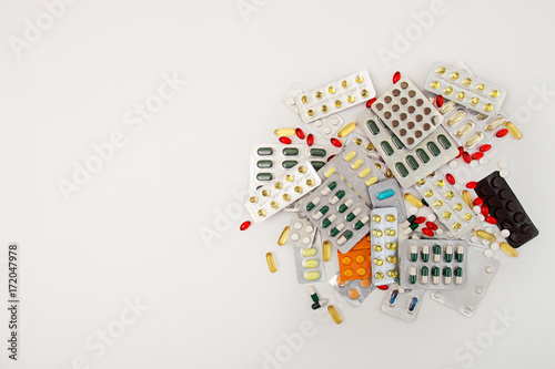 Heap of medicine tablets and pills in blisters different colors on white background. Healthcare or medicament addiction concept. Copy space.