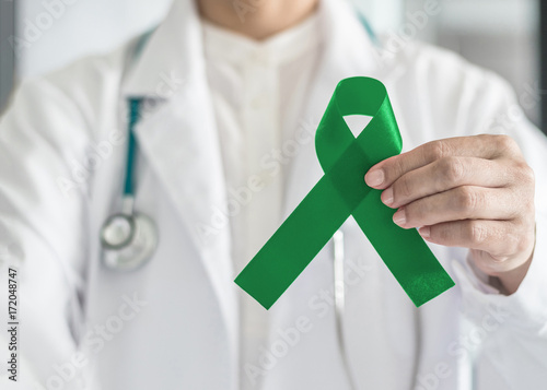 Jade (emerald) green ribbon in doctor's hand for Liver Cancer and hepatitis B awareness concept . photo