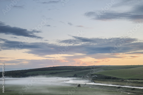 Beautiful dawn landscape over English countryside with river slowly flowing through fields