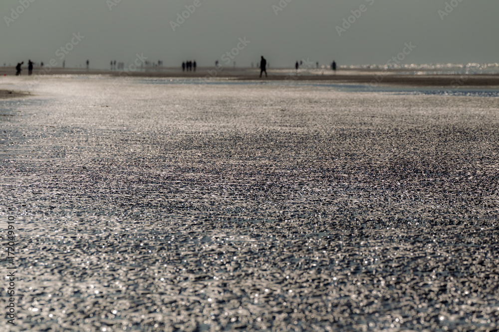 Die Sonne spiegelt sich im flachen Wasser am Strand der Nordseeinsel Juist in Ostfriesland, Deutschland, Europa.