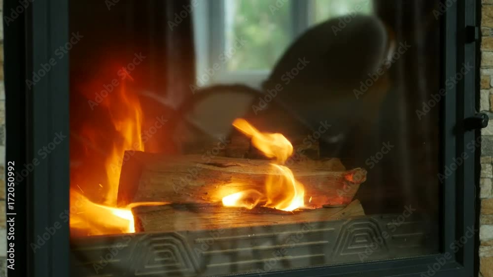 Fireplace burning. Warm cozy fire in a modern fireplace close up. Cozy background of firewood is burning in the fireplace with a reflection of rocking chair in glass Fireplace burning. Warm cozy fire in a modern fireplace close up. Cozy background of firewood is burning in the fireplace with a reflection of rocking chair in glass