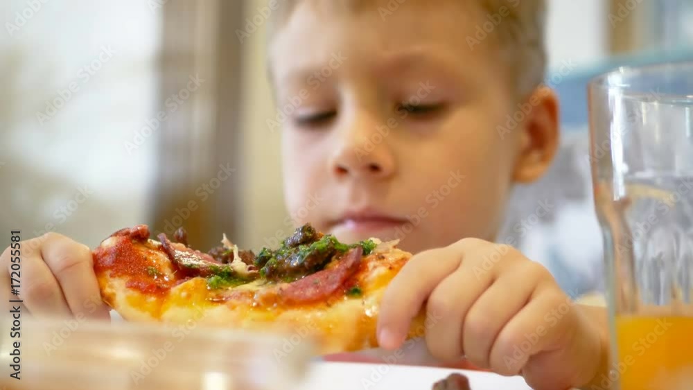 Close up of little cute boy eating pizza. Selective focus on pizza with meat, cheese and sausage. Five year old boy eating a slice of pepperoni pizza. Close up of little cute boy eating pizza. Selective focus on pizza with meat, cheese and sausage. Five year old boy eating a slice of pepperoni pizza.