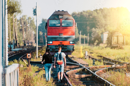 A guy and a girl are walking towards the train by a locomotive on the railway