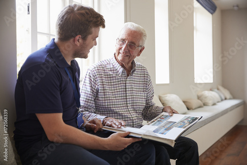 Senior man sitting looking at photo album  with male nurse photo