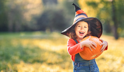 child girl with pumpkin outdoors in halloween
