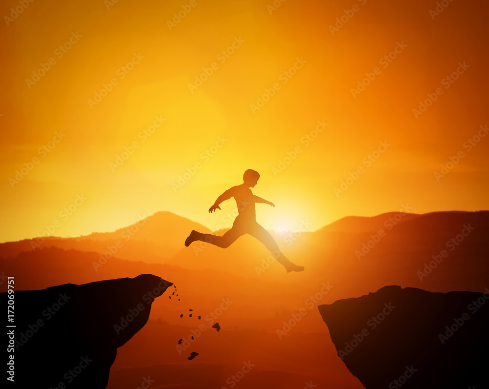Man jumping from one rock to another. Sunset mountains scenery