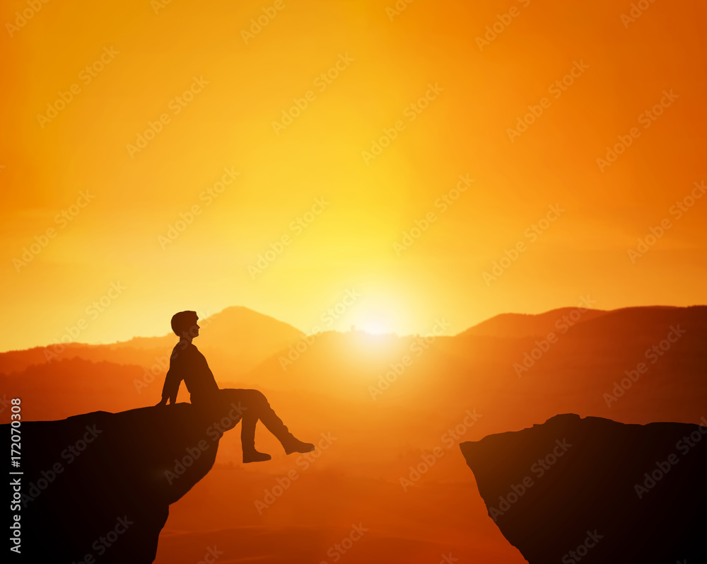 Man sitting relaxed on the edge of mountain looking at scenic sunset skyline.