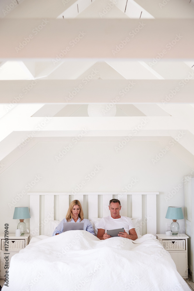 Couple Wearing Pajamas Lying In Bed Using Digital Devices Couple Wearing Pajamas Lying In Bed Using Digital Devices