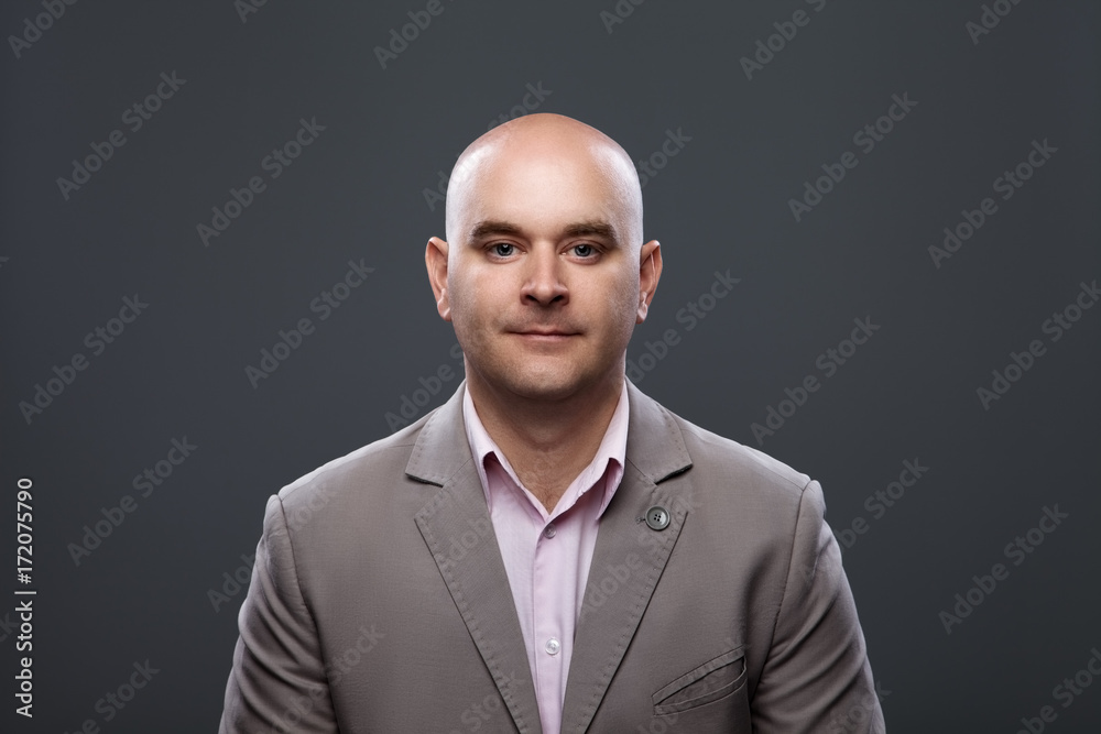 Portrait of a bald affable man in a suit against a dark background Portrait of a bald affable man in a suit against a dark background