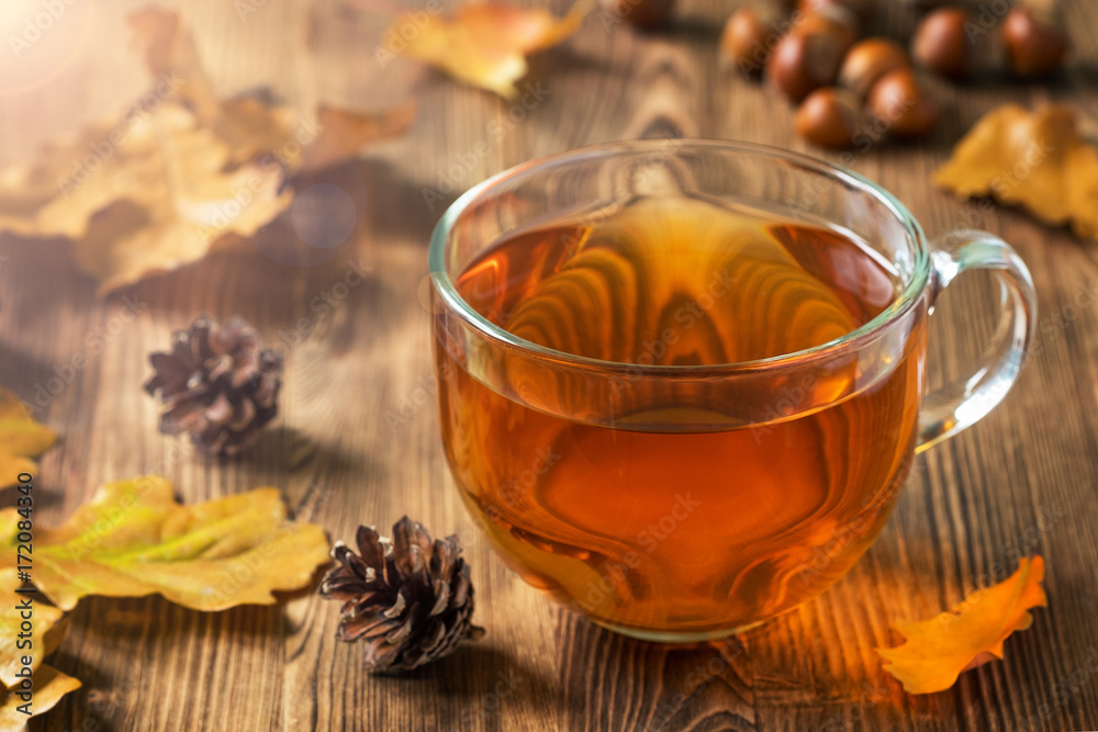 Fototapeta premium Cup of tea with autumn leaves and pine cones on a wooden table.