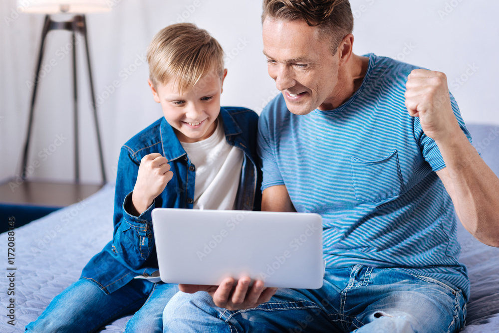 Joyful father and son celebrating goal while watching football online Joyful father and son celebrating goal while watching football online