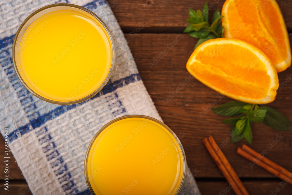 Orange juice in a glass on a wooden background with orange and melissa and cinnamon. Top view. Orange juice in a glass on a wooden background with orange and melissa and cinnamon. Top view.