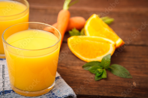 Refreshing orange-carrot juice in a glass on a wooden background. Carrots, orange, mint, Melissa and fruit and vegetable juice. Vitamins. Proper nutrition.