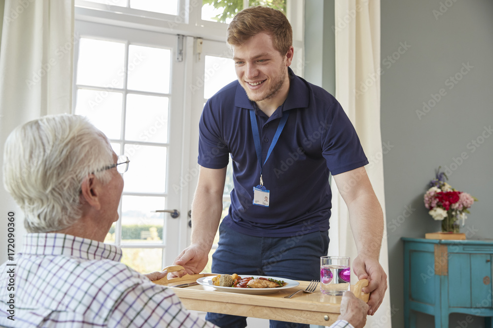 Male care worker serving dinner to a senior man at his home - obrazy, fototapety, plakaty 