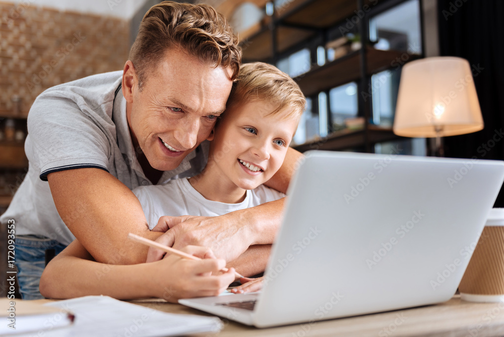 Happy father cuddling son while he doing homework