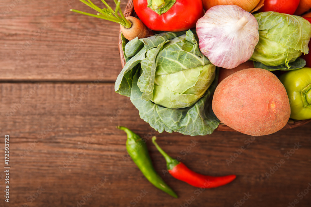 Fresh vegetables in a basket on a wooden background. Cabbage, bell pepper, potatoes, garlic, onion, chili and carrots. Harvest. Thanksgiving Day. Space for text.