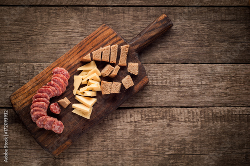 Cutting board with Salami, cheese and bread on dark wooden background