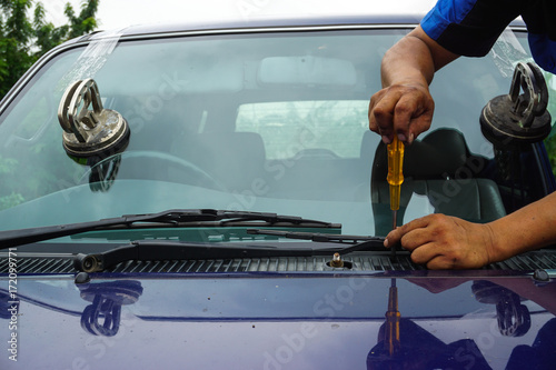 Glazier using tools repairing to fix crack broken windshield, windscreen on the front window glass of the machine car accident.
