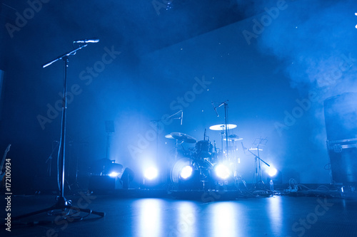 A kit of drums and a microphone on an empty stage in blue smoke before the concert