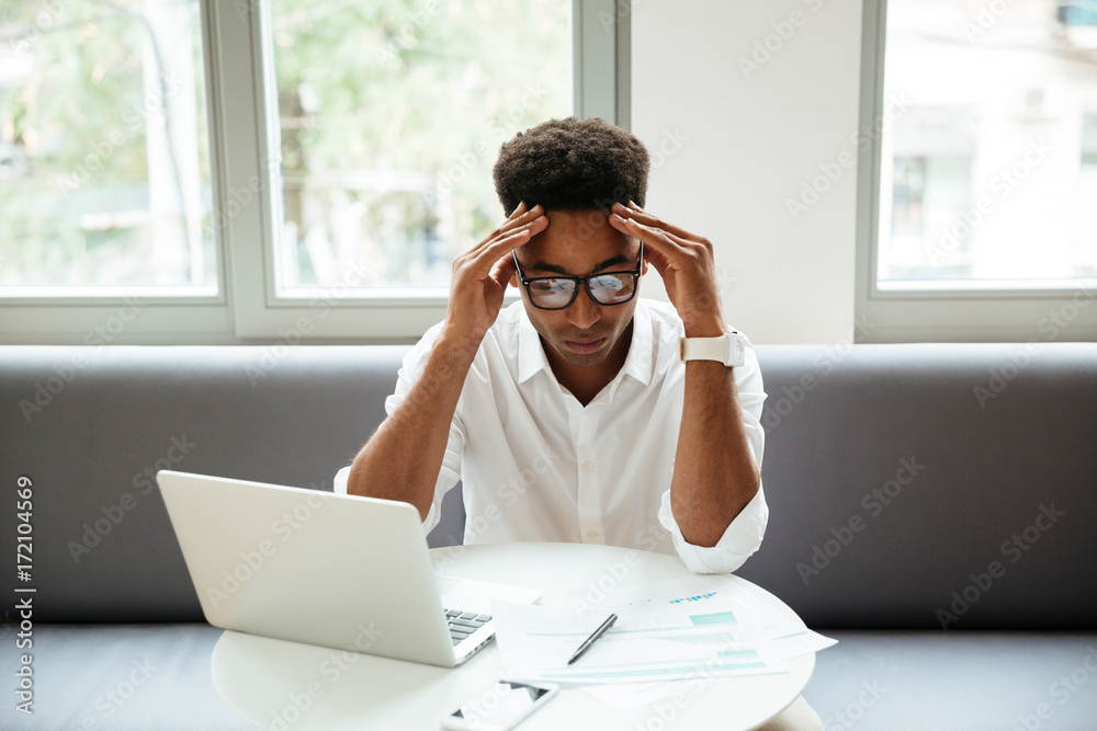 Concentrated serious young african man sitting coworking Concentrated serious young african man sitting coworking