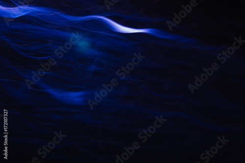 Abstract background of white waves in motion on black. Bokeh of defocused curves, blurred neon leds, similar to tobacco smoke, backdrop of addictions and acquired habits