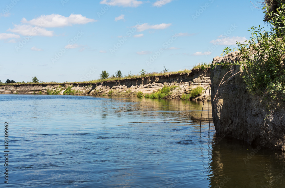 Steep sand shore of the river; Reflections of the sky and steep bank in the water