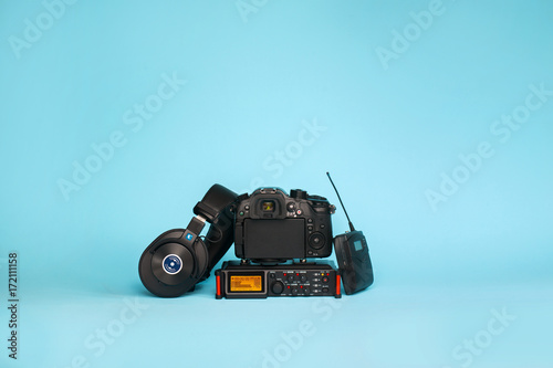 equipment for field video production, camera, boom mic, recorder and wireless system on blue background