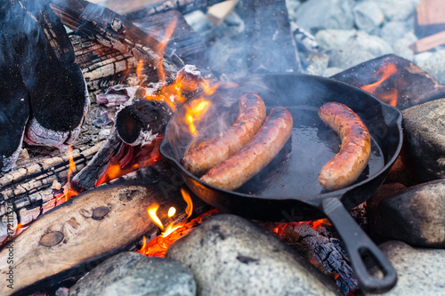 Fotografi Cooking sausages in cast iron skillet on campfire while camping