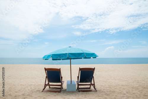 Fototapeta Naklejka Na Ścianę i Meble -  Beach chairs and blue umbrella on beautiful sand beach with cloudy and blue sky