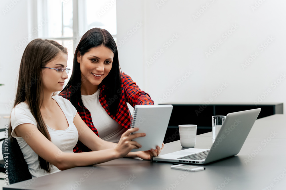 Two businesswomen consulting a report together on a desk at the office. Two businesswomen consulting a report together on a desk at the office.
