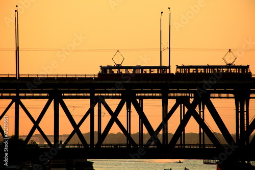 Obraz na plátně Silhouettes of a two-tiered bridge and 2 trams on a sunset ,  Dnepr city, (Dnepr