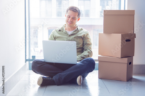Handsome man with moving boxes and laptop sitting on stairs