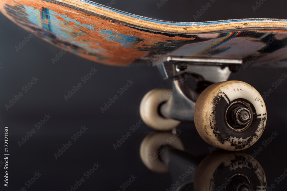 Partially seen skateboard on black glance background. Rubbed deck and