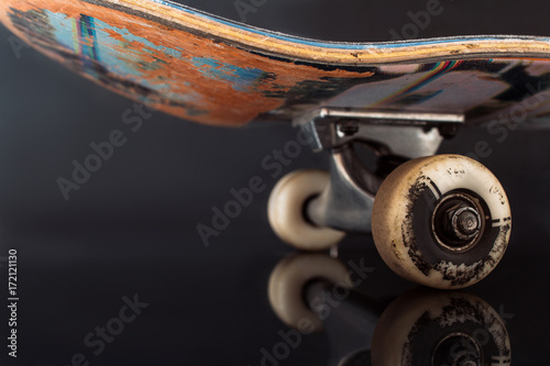 Partially seen skateboard on black glance background. Rubbed deck and wheels of professional extreme sport device, advertizing of safety consrtuction and fastness to rubbing of elements, free space photo