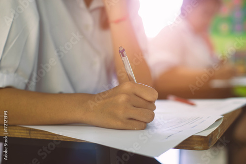 Closeup to hand of student holding pen and taking exam in classroom with stress for education test .