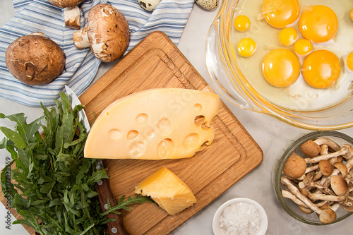 Overhead of ingredients frittata quiche vegeterian diet meal. Eggs in bowl, quail eggs, milk, cheese mozzarella, gouda, tomato, spinach, mushrooms, champignon, Honey fungus, arugula photo