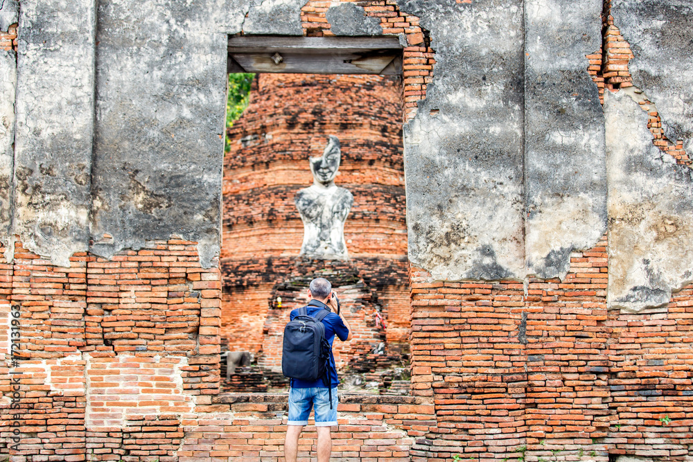A professional male photographer with bag a camera and taking photos in front of old temple urban wall background at Ayutthaya Province, Thailand A professional male photographer with bag a camera and taking photos in front of old temple urban wall background at Ayutthaya Province, Thailand