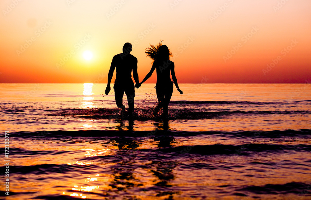 Silhouette of young fitness couple walking inside the water at sunrise - Multi race people having fun on vacation - Romantic and love concept - Soft focus on man - Sun color tones filter