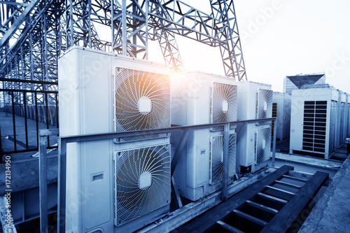 Air conditioner units (HVAC) on a roof of industrial building with blue sky and clouds in the background. photo