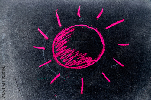 Red chalk drawing as sun with ray on black board background