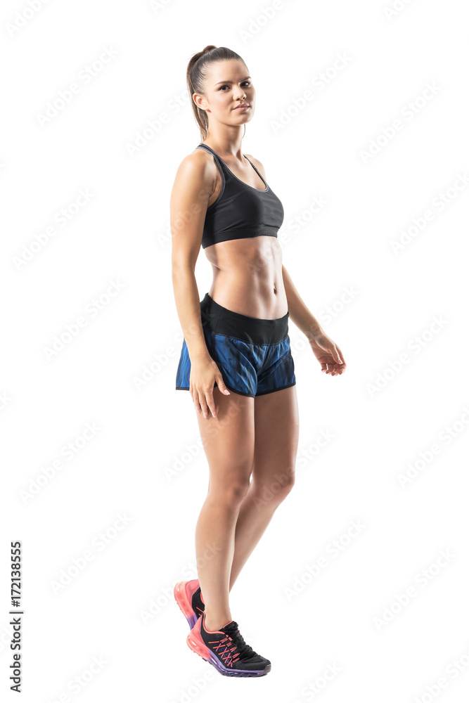 Side view of relaxed young fitness woman walking and looking at camera. Full body length portrait isolated on white studio background. Side view of relaxed young fitness woman walking and looking at camera. Full body length portrait isolated on white studio background.