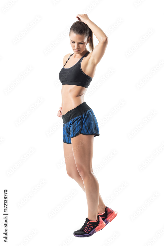 Side view of gorgeous fitness female model posing with hand in hair looking down. Full body length portrait isolated on white studio background. Side view of gorgeous fitness female model posing with hand in hair looking down. Full body length portrait isolated on white studio background.
