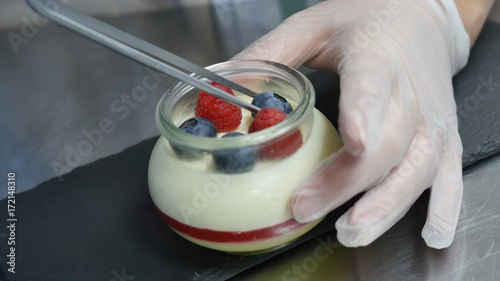 Homemade yogurt with blueberries in a glass jar. Hand putting Strawberry in Yogurt, close up photo