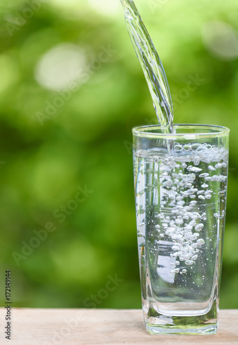 Pouring fresh water into glass on wood table with green nature background