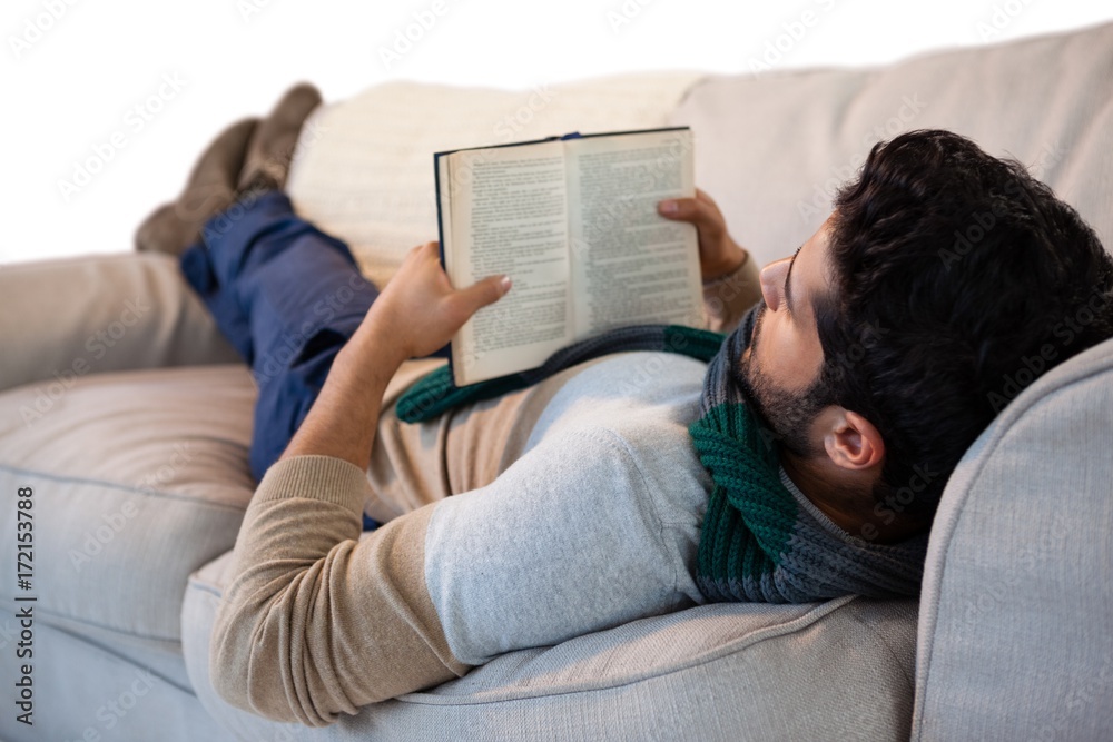 Obraz premium Man lying on sofa while reading book