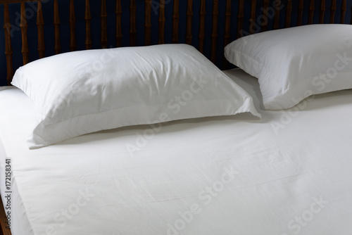 White pillows and bedding in blue bedroom interior in morning time with alarm clock on wooden bed side table