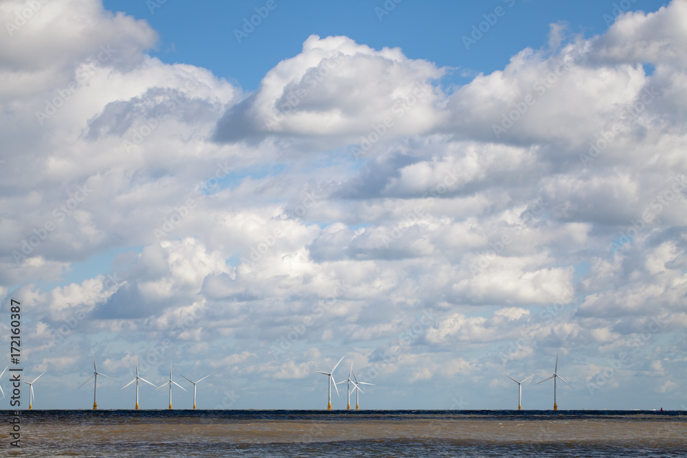 Offshore wind farm on horizon beneath cloudy sky.