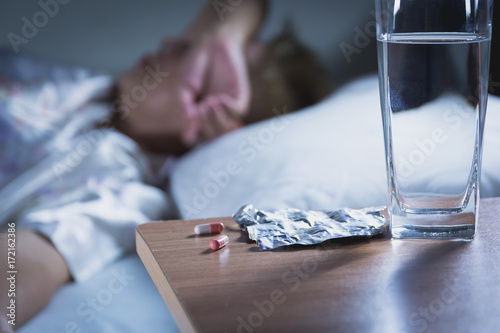 Sick woman takes capsule pill and drink water before sleeping for rest.