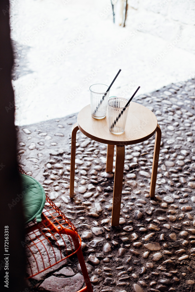Two empty glasses or jars of coffee, juice or lemonade with straws stand symmetrically on wooden table in front of cafe or bar in old town of dubrovnik